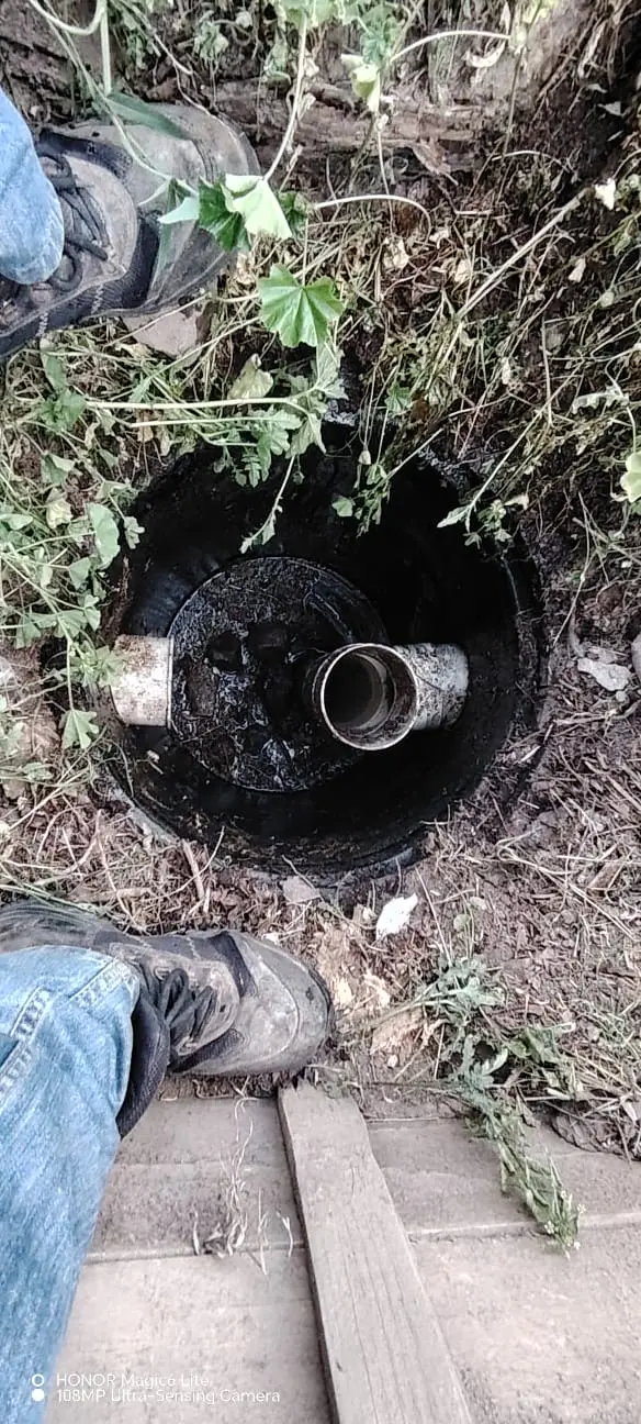 Vista aérea de una caja de revisión de alcantarillado abierta con tuberías obstruidas, siendo inspeccionada por personal técnico de Saneamiento RAMGL para su limpieza.