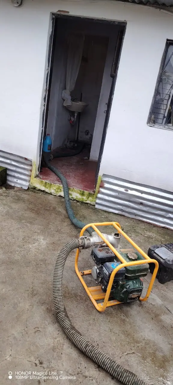 Una motobomba con mangueras de succión conectadas que se extienden hasta el interior de un cuarto con un lavabo, para realizar la limpieza de trampas de grasa.