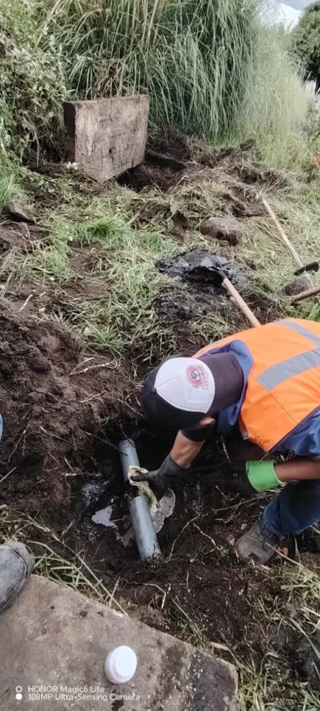 Técnico de Saneamiento RAMGL realizando la reparación y destape de tuberías de desagüe subterránea en una zona de terreno natural para asegurar el flujo correcto hacia la red de alcantarillado.