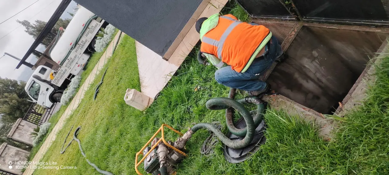 Técnico de Saneamiento RAMGL con chaleco de seguridad realizando la succión y limpieza de una cisterna subterránea utilizando maquinaria especializada y mangueras de alta resistencia.