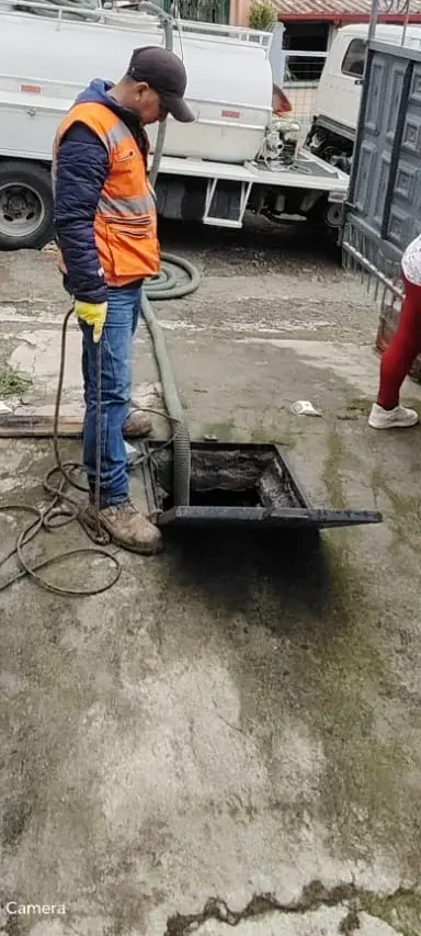 Operario de Saneamiento RAMGL supervisando la limpieza de una cisterna residencial mediante un sistema de succión conectado a un camión cisterna especializado.