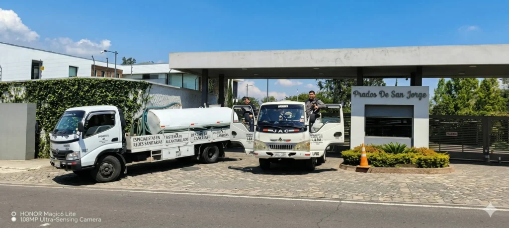 1. Texto alternativo (Alt Text) Camiones cisterna de Saneamiento RAMGL operando en urbanización de Sangolquí, especialistas en limpieza de pozos sépticos.