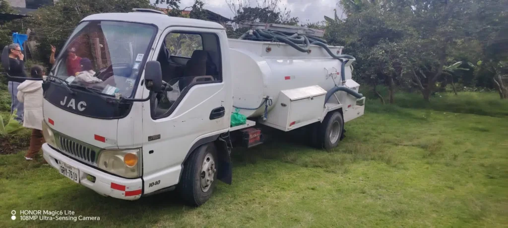 Camión de succión compacto de Saneamiento RAMGL realizando limpieza de pozo séptico en zona residencial periférica de Quito.