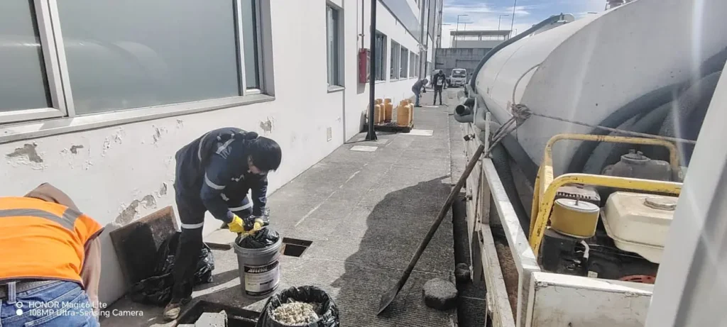 Personal técnico especializado realizando la extracción y recolección de residuos sólidos y  limpieza de trampas de grasa, nspección en un pasillo industrial externo, utilizando cubetas, bolsas de basura y equipo de succión.