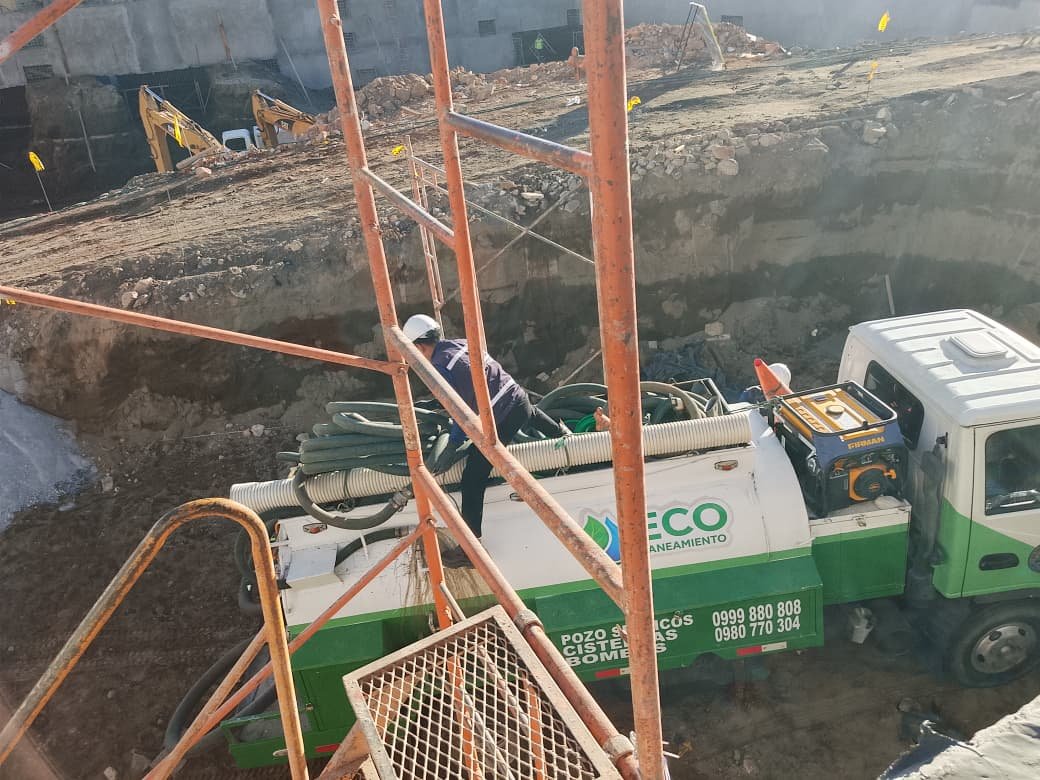 Limpieza de pozos sépticos en obra de construcción con camión hidrosuccionador y operario con casco manipulando las mangueras de succión